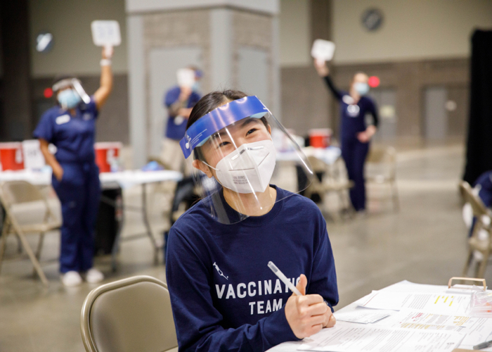 A person in a face shield smiles for a photo at a vaccination station
